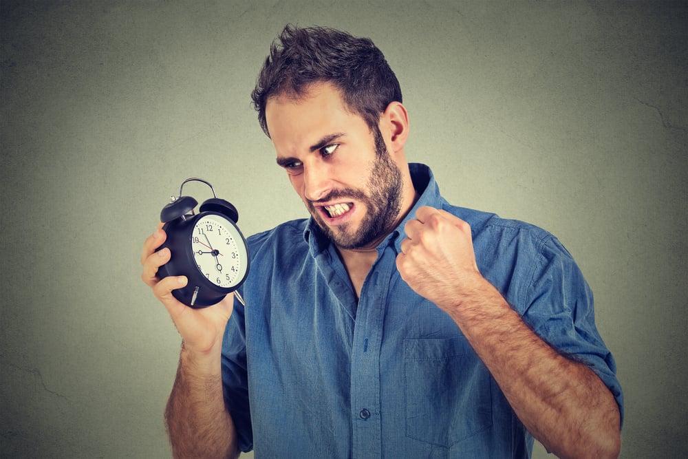 Portrait upset angry young man screaming at alarm clock isolated on gray wall background. Employee running late. Time management concept