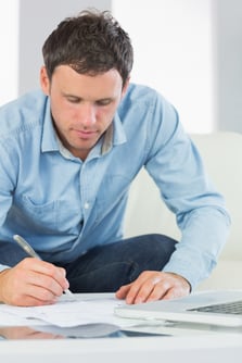 Content casual man writing on sheets paying bills in bright living room